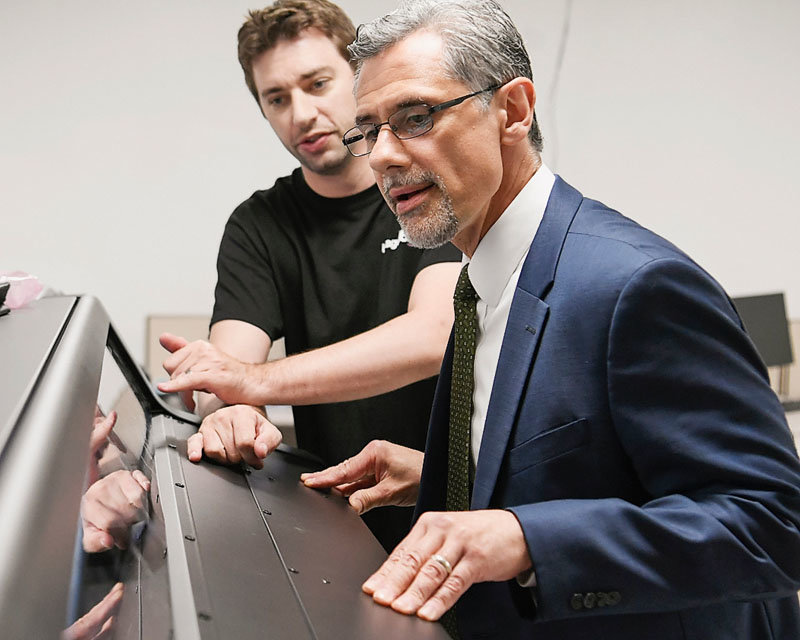 Daily Gazette publisher John DeAugustine listens as Chris Miller of Image360 explains the operations of a sign printer in this May 2019 file photo.